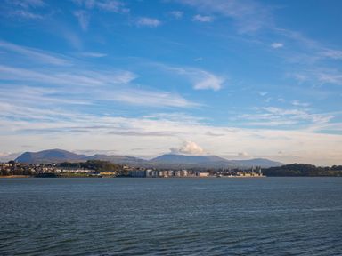 A body of water with a town and mountains in the background at The Mermaid in Brynsiencyn