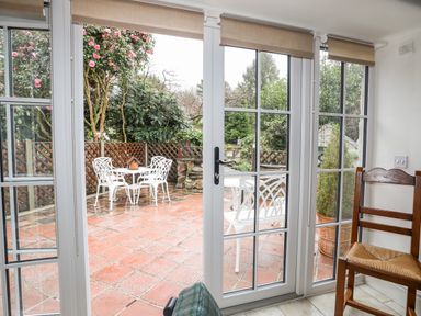 A patio with white table and chairs surrounded by plants outside glass doors with brown blinds at The Honey Pot in Garndolbenmaen