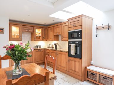 A kitchen with wooden cabinets dining table with flowers and a bench with baskets at The Honey Pot in Garndolbenmaen