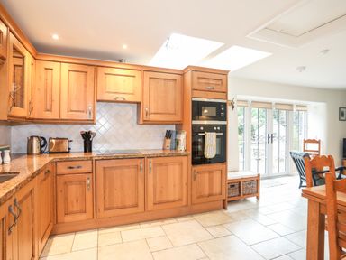 A kitchen with wooden cabinets stone countertops a built in oven microwave a toaster kettle and dining area at The Honey Pot in Garndolbenmaen