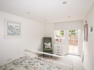 A bedroom with a bed a green armchair a white bedside table with flowers and a door leading outside at The Honey Pot in Garndolbenmaen