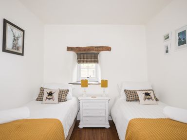 A bedroom with two single beds a small white bedside table with lamps and framed pictures on the walls at The Honey Pot in Garndolbenmaen