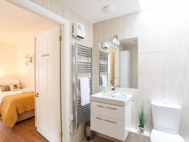 A bathroom with a white sink cabinet mirror towel rack and toilet next to a bedroom at The Honey Pot in Garndolbenmaen