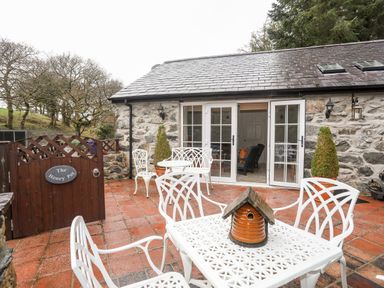 A stone patio with white metal table and chairs a wooden gate and potted plants at The Honey Pot in Garndolbenmaen