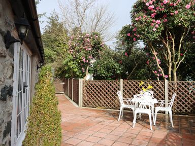 An outdoor patio with white metal table and four chairs surrounded by a brown lattice fence and flowering trees at The Honey Pot in Garndolbenmaen