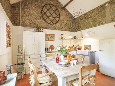 A kitchen with a wooden table and chairs a white refrigerator and stone walls at Three Gates in Llangoed