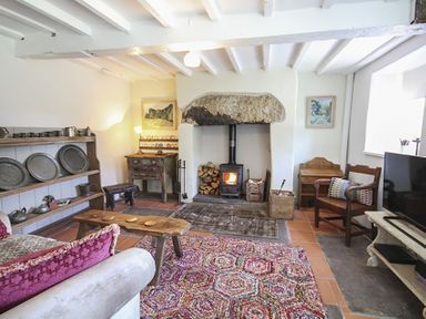 A living room with a wood burning stove wooden furniture and shelves with pewter plates and mugs at Three Gates in Llangoed