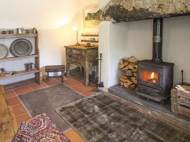 A room with a wood burning stove a small wooden table shelves with metal dishes and a wooden stool at Three Gates in Llangoed