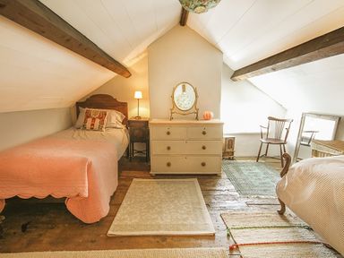 An attic bedroom with two beds a wooden chair a chest of drawers with a mirror and rugs on a wooden floor at Three Gates in Llangoed
