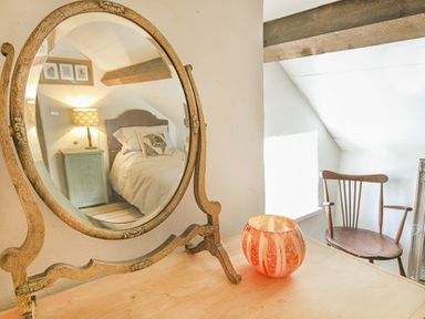A wooden table with a round mirror and a decorative candle holder with a chair and bed reflected in the mirror at Three Gates in Llangoed