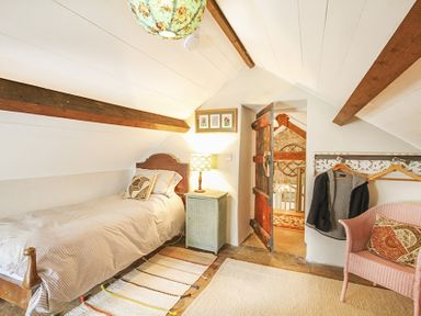 A small bedroom with a single bed a bedside table and lamp an open wooden door a pink chair and coat hooks with clothes at Three Gates in Llangoed