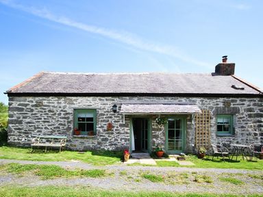 A stone cottage with green window frames and doors and outdoor seating at Three Gates in Llangoed