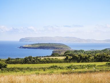 A coastal landscape with grassy fields and sea with islands in the distance at Three Gates in Llangoed