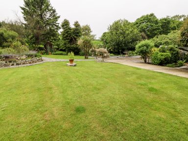 A garden with a lawn stone paths and various trees and shrubs at The Little Coach House in Garndolbenmaen