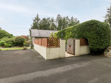 An outdoor area with a wooden gate and lattice fencing surrounded by tall trimmed hedges and trees at The Little Coach House in Garndolbenmaen