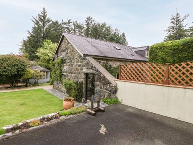 Stone house with slate roof next to lawn and wooden fence at The Little Coach House in Garndolbenmaen