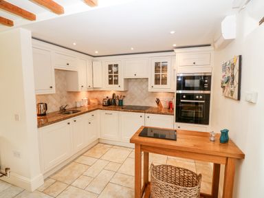 A kitchen with white cabinets a wooden table and tiled floor at The Little Coach House in Garndolbenmaen