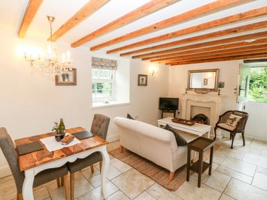 A living room with a sofa a dining table and chairs a fireplace and exposed wooden ceiling beams at The Little Coach House in Garndolbenmaen