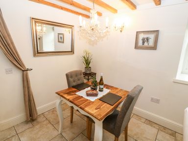 A dining area with a wooden table two upholstered chairs a chandelier and wall art at The Little Coach House in Garndolbenmaen