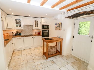 A kitchen with white cabinets wooden beams on the ceiling and a wooden table with a basket at The Little Coach House in Garndolbenmaen