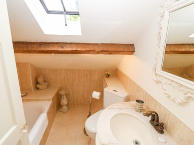 A bathroom with a skylight wooden beam a bathtub a toilet a sink and a decorative mirror at The Little Coach House in Garndolbenmaen