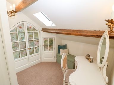 A small room with a white vanity desk and chair a skylight wooden beam and a green bench with pillows at The Little Coach House in Garndolbenmaen