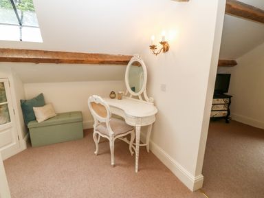 A corner with a white dressing table and chair next to a green storage bench with cushions at The Little Coach House in Garndolbenmaen