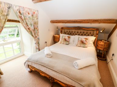 A bedroom with a bed two bedside tables lamps a window and floral curtains at The Little Coach House in Garndolbenmaen