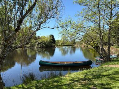 A pond with a canoe and a boat by the grassy shore surrounded by trees at The Little Coach House in Garndolbenmaen
