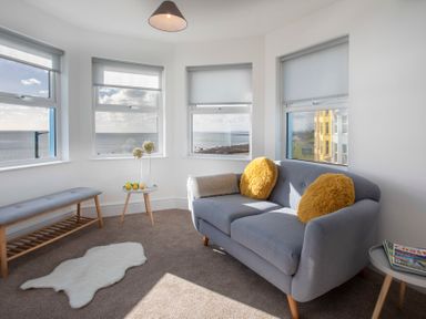 A sitting room with a grey sofa and yellow cushions by windows showing an ocean view at The Towers - Ardudwy in Criccieth