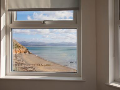 A window showing a beach with a cliff and calm sea at The Towers - Ardudwy in Criccieth