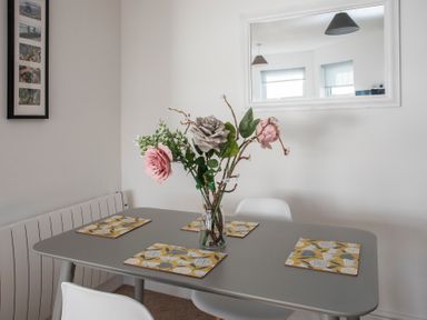 A dining table with floral placemats and a vase with flowers in a room with a wall mirror and framed pictures at The Towers - Ardudwy in Criccieth