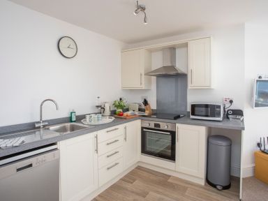 A kitchen with white cabinets a gray countertop a sink dishwasher oven stovetop microwave and trash bin at The Towers - Ardudwy in Criccieth