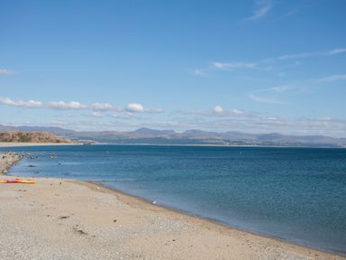 A beach with sand and pebbles next to a calm sea with hills in the background at The Towers - Ardudwy in Criccieth