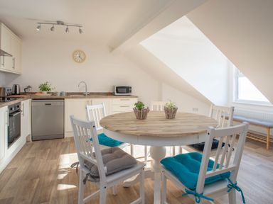 A kitchen with a round wooden table with chairs and cushions at The Towers - Castell in Criccieth