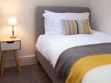 A bedroom with a bed featuring white bedding and a patterned pillow next to a wooden nightstand with a lamp at The Towers - Castell in Criccieth