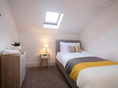 A small bedroom with a bed a bedside table with a lamp and a chest of drawers with a plant at The Towers - Castell in Criccieth
