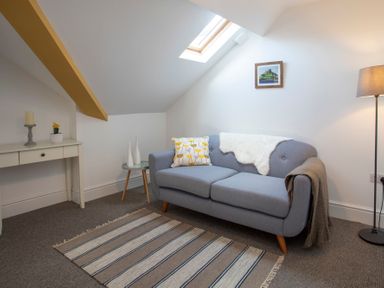 A living room with a gray sofa a side table a floor lamp and a small desk at The Towers - Castell in Criccieth