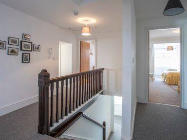 A hallway with carpeted floor, wooden banister, framed pictures on the wall, and doorways leading to other rooms at The Towers - Castell in Criccieth