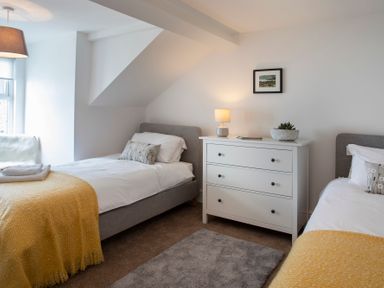 A bedroom with two single beds a white dresser with a lamp and a plant and a window with a pendant light at The Towers - Castell in Criccieth
