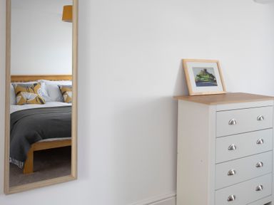 A bedroom reflected in a wall mirror showing a bed with patterned pillows and a blanket and a white chest of drawers with a framed picture on top at The Towers - Castell in Criccieth
