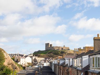 A row of houses with chimneys and rooftops with a stone castle on a hill in the background at The Towers - Castell in Criccieth