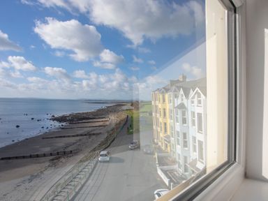 A view of a beach and a row of colorful houses seen through a window at The Towers - Castell in Criccieth