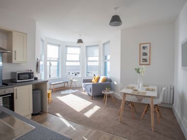 A living and dining area with a sofa by windows overlooking water at The Towers - Llyn in Criccieth