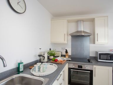 A kitchen countertop with a sink dishwashing liquid cups kettle cutting board with vegetables and eggs oven stovetop microwave and cabinets at The Towers - Llyn in Criccieth