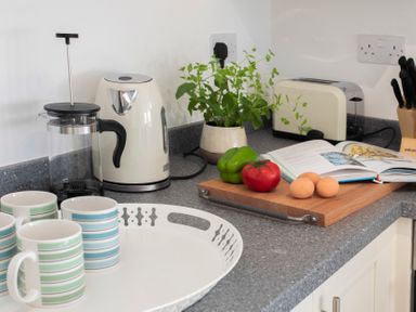 A kitchen countertop with a French press kettle cups cutting board vegetables cookbook and knife block at The Towers - Llyn in Criccieth