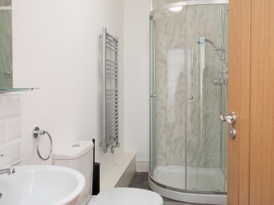 A bathroom with a toilet, sink, glass shower enclosure, and towel radiator at The Towers - Llyn in Criccieth