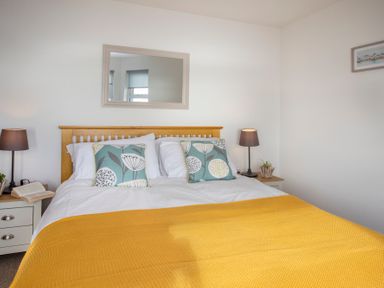 A bedroom with a wooden bed frame yellow blanket and two bedside tables with lamps at The Towers - Llyn in Criccieth