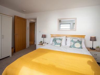 A bedroom with a wooden bed frame a yellow blanket patterned pillows two bedside tables with lamps and a wardrobe at The Towers - Llyn in Criccieth