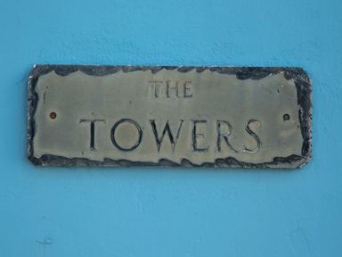 A weathered sign with the text THE TOWERS mounted on a blue wall at The Towers - Llyn in Criccieth